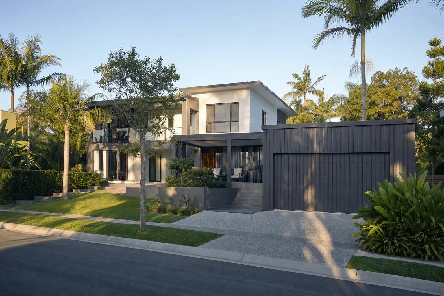 Dark garage shed joined by a patio to a modern two-storey home in Robina