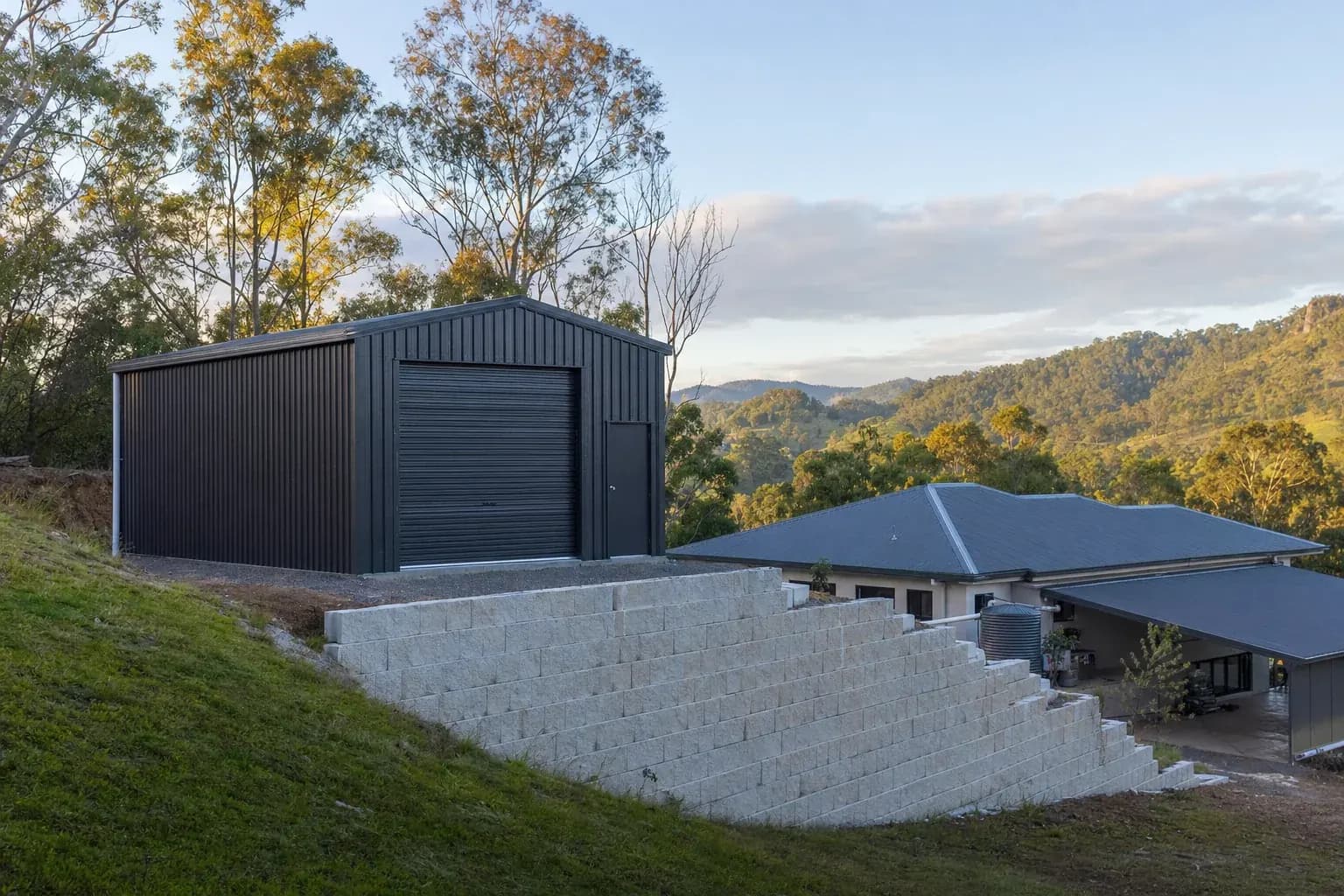 Charcoal workshop shed on a cut pad above a block retaining wall on a sloping Upper Coomera lot